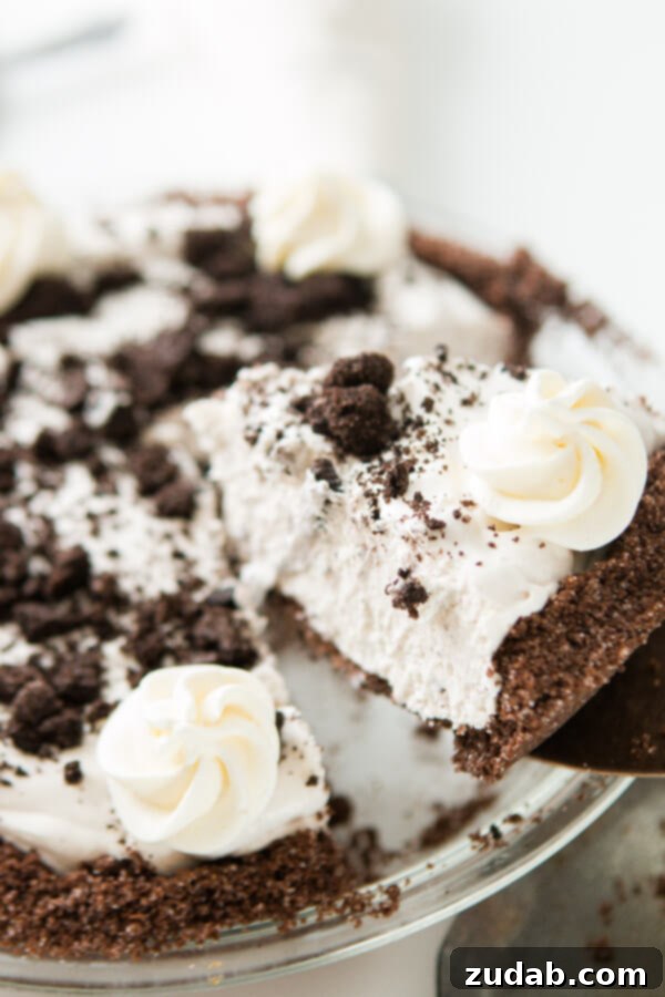 This is one of our most popular pie recipes and it's an easy pie recipe! Who wants a slice of no bake oreo pie with chocolate graham cracker crust?! Picking up a piece of oreo cookie pie with chocolate graham cracker crust with a cake knife.