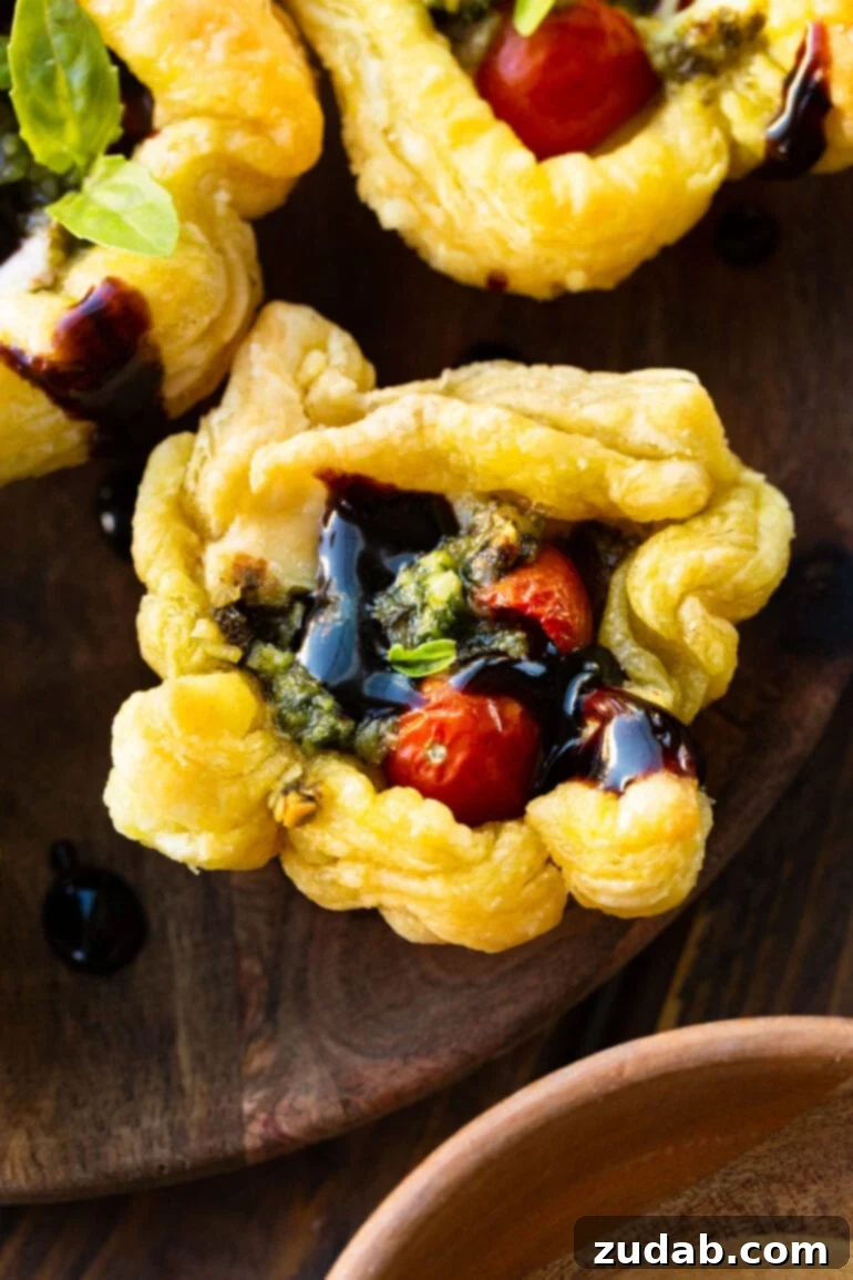 Speedy Cheesy Caprese Pesto Tarts 3 A perfectly golden baked puff pastry pesto cup, artfully garnished with a shimmering balsamic glaze and a sprig of fresh basil. This image captures the appetizing warmth and elegant presentation of the finished tart.