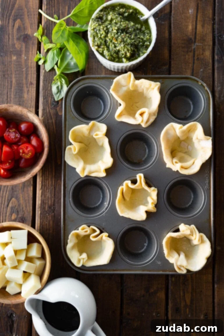 Speedy Cheesy Caprese Pesto Tarts 5 A clear photo of unbaked puff pastry rounds, meticulously pressed into a mini muffin pan, showcasing the preparation stage for easy Caprese pesto tarts.