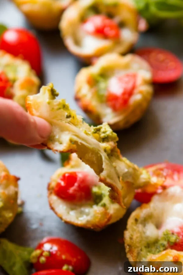 Speedy Cheesy Caprese Pesto Tarts 9 A close-up of several unbaked Caprese pesto tarts neatly arranged in a mini muffin pan, carefully covered with plastic wrap, illustrating the perfect make-ahead storage method for future baking.