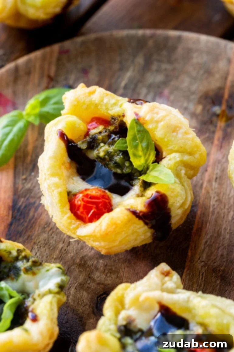 Speedy Cheesy Caprese Pesto Tarts 10 A vibrant photo of a golden baked Caprese pesto tart, beautifully topped with a glistening balsamic glaze and a plump cherry tomato, ready for serving.