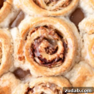 A photo taken over the top of a pan of golden baked apple cinnamon rolls topped with a sweet glaze