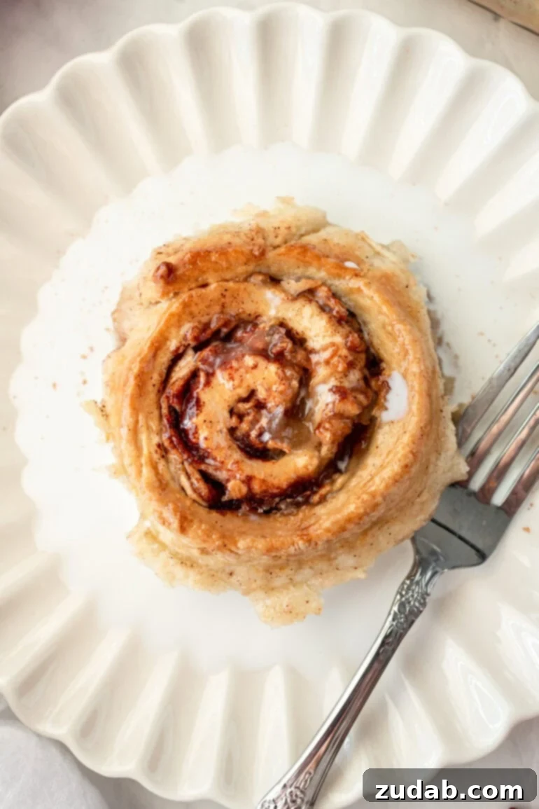 Rustic Orchard Apple Swirls 3 A single, golden-baked heirloom apple roll with a delicate glaze, resting in a shallow dish of warm cream, highlighting its simple, timeless ingredients.