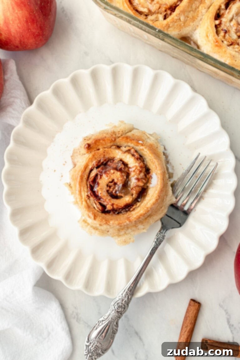 Rustic Orchard Apple Swirls 9 A perfectly baked apple cinnamon roll, cut with a fork, revealing its warm, spiced apple filling, served in a thin layer of cream.