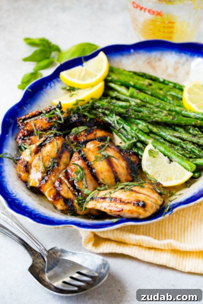 A photo of a blue plate with several grilled chicken thighs on it with a side of grilled asparagus and slices of lemon.