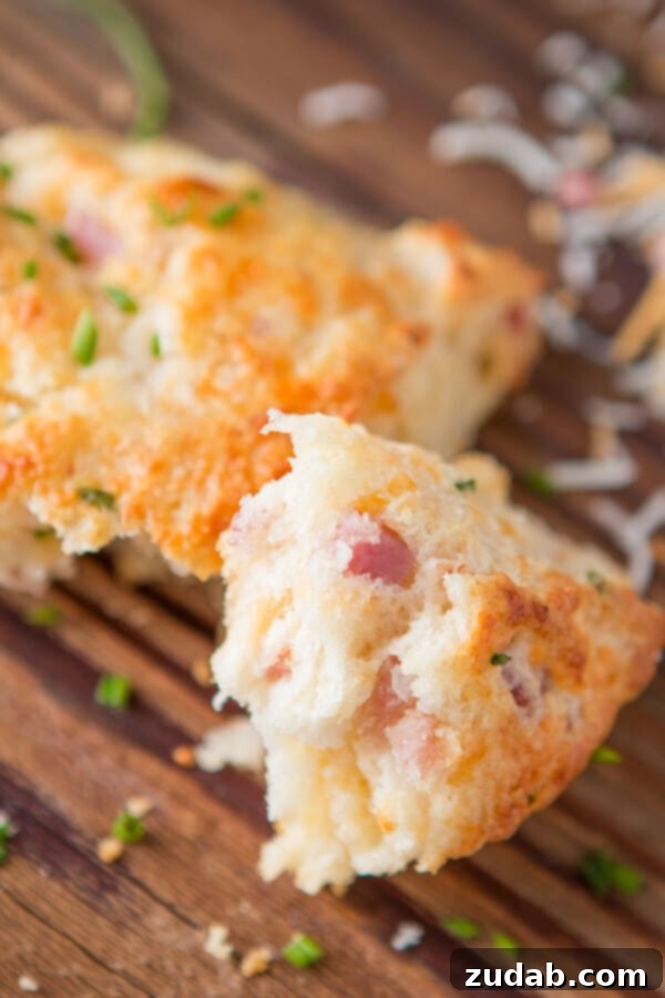 A few weeks ago I was making our apple pie scones and suddenly had the brilliant idea of making a savory version, easy ham and cheese scones! a photo of a chunk of flakey and tender ham and cheese scone sitting on a wooden cutting board so you can see the inside of the golden scone
