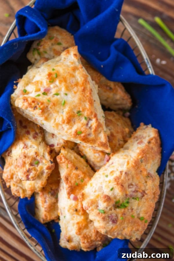 A few weeks ago I was making our apple pie scones and suddenly had the brilliant idea of making a savory version, easy ham and cheese scones! a photo of a metal wire basket lined with a blue cloth and full of golden baked ham and cheese scones.