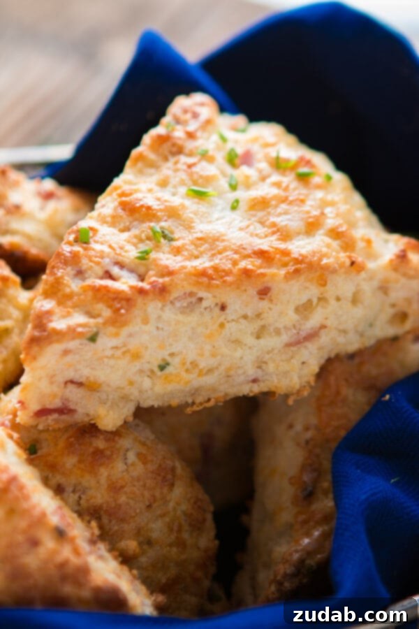 A few weeks ago I was making our apple pie scones and suddenly had the brilliant idea of making a savory version, easy ham and cheese scones! a close up photo of a baked golden fluffy scone load with chunks of cheese and ham and brushed on top with butter and sprinkled with chopped chives