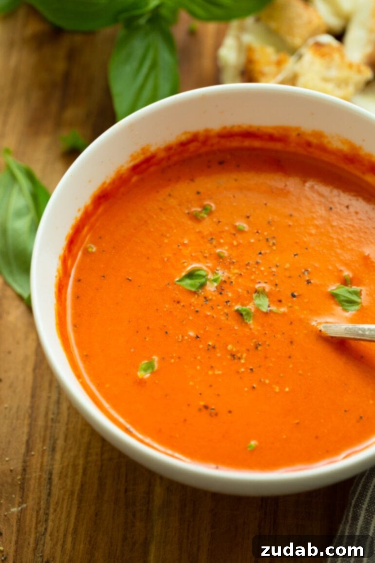 Comforting Roasted Tomato Basil Soup with Grilled Cheese Bites 5 A cozy bowl of bright orange-red homemade tomato basil soup, generously topped with fresh minced basil and freshly cracked black pepper.