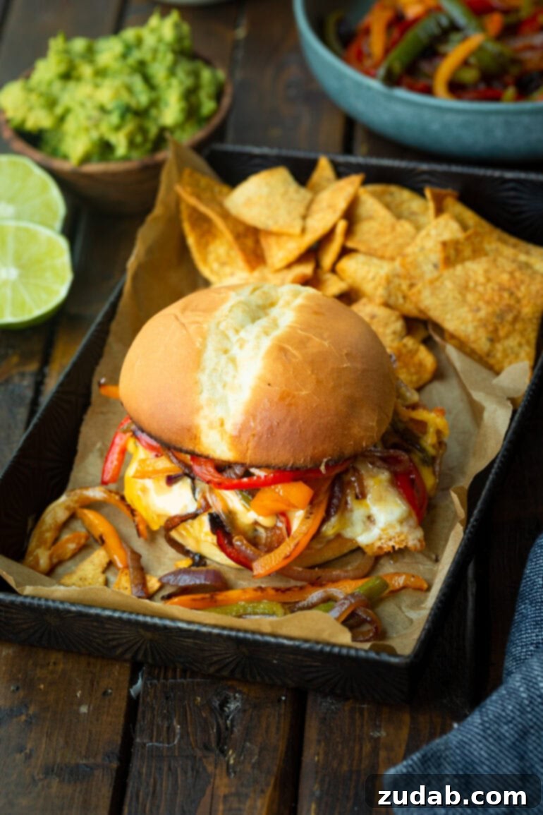 A mouth-watering fajita turkey burger, richly loaded with melted gooey cheese, sautéed peppers and onions, and a creamy sauce, with a pile of tortilla chips blurred in the background.