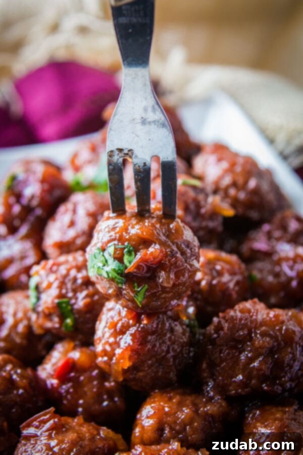 Fork spearing a juicy grape jelly meatball, highlighting its saucy coating