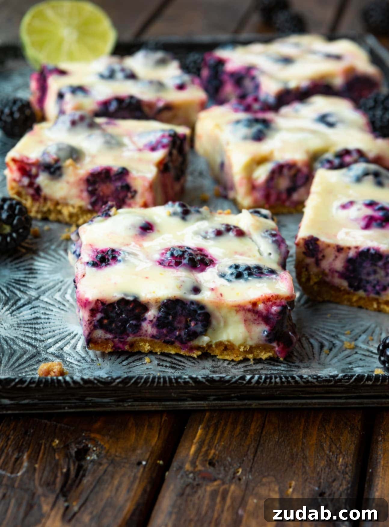 Zesty Blackberry Lime Bars 3 A photo of several blackberry lime bars sitting on a serving tray, showcasing their perfectly baked graham cracker crust and plump, rich purple blackberries embedded in the creamy lime filling.