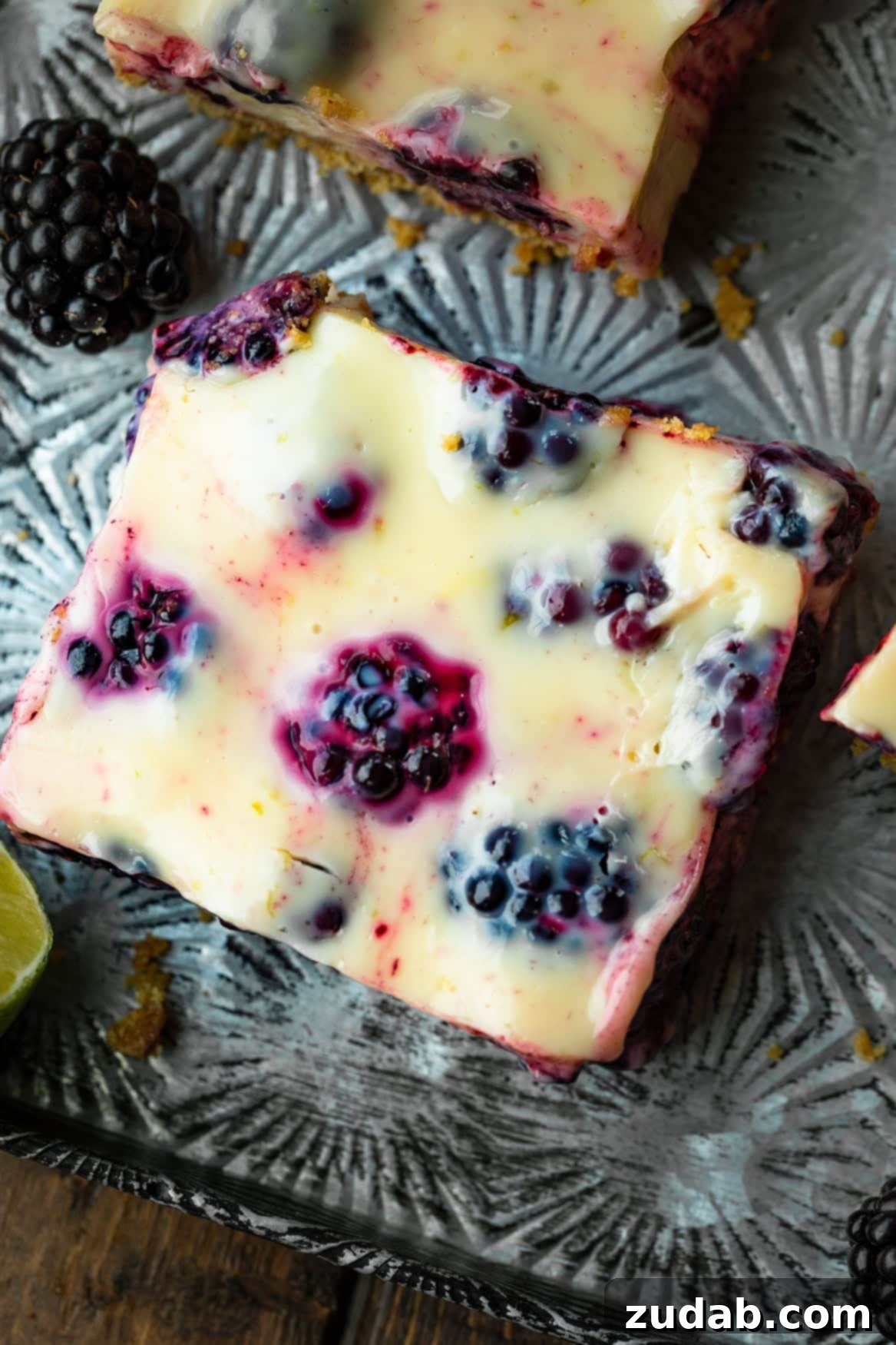 Zesty Blackberry Lime Bars 7 A close-up photo of a single, delectable blackberry lime bar, revealing its thick graham cracker crust, creamy lime filling, and abundant fresh blackberries perfectly nestled within.