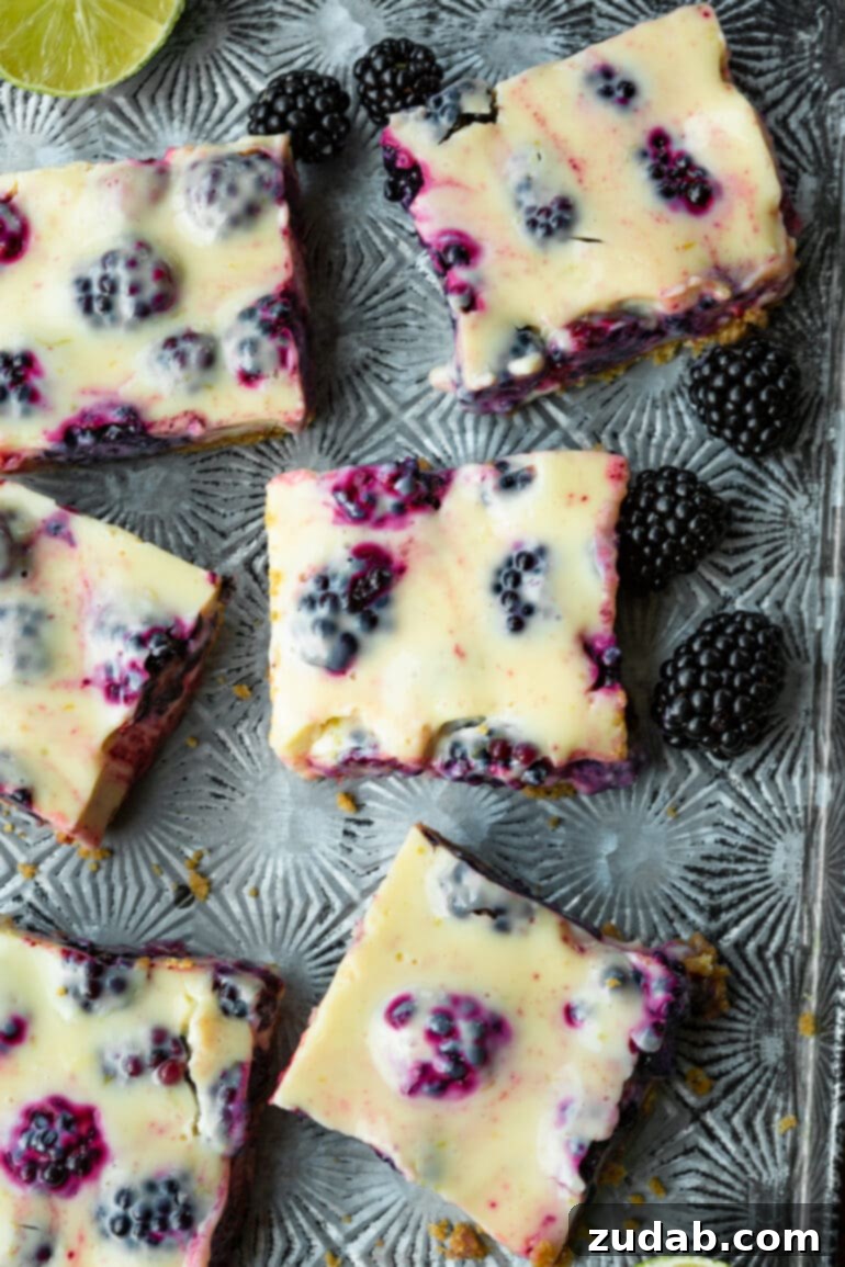 Zesty Blackberry Lime Bars 10 A photo of several blackberry lime bars arranged on a metal serving tray, artfully scattered with fresh, vibrant blackberries, creating an inviting visual of a delightful dessert.