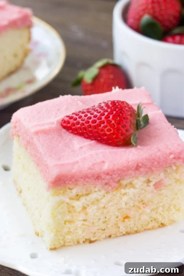 Delicious Vanilla Cake with Fresh Strawberry Frosting A slice of moist vanilla cake topped with delicate pink strawberry buttercream and a fresh strawberry half, showcasing the perfect spring dessert.
