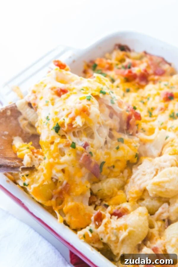Enjoy a generous serving of this quick and easy Cheesy Chicken Bacon Ranch Casserole, a perfect family meal! ohsweetbasil.com A close-up of a serving of Cheesy Chicken Bacon Ranch Casserole being spooned out, showing the melted cheese and pasta.
