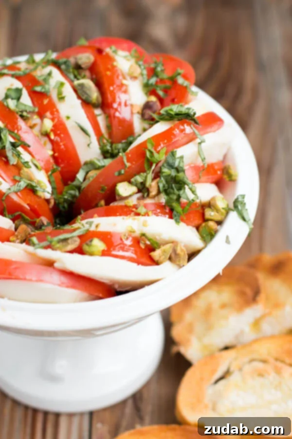 Effortless Caprese Delight 5 A stunning Caprese Salad featuring thick slices of fresh mozzarella and ripe red tomatoes, layered with vibrant basil and sprinkled with crunchy pistachios, served on a white plate.