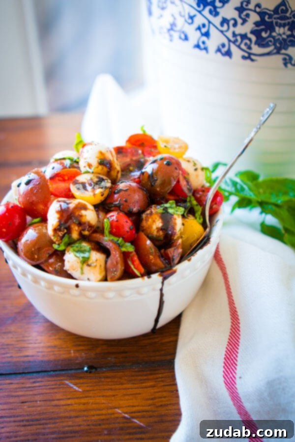 Tomato Mozzarella Salad with Balsamic Glaze A beautifully composed bowl of easy tomato mozzarella salad, featuring cherry tomatoes, marinated mozzarella pearls, and fresh basil leaves, artfully drizzled with a homemade balsamic reduction.