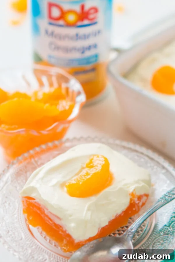 A classic Lemon Mandarin Orange Jello Salad, perfect for holiday meals, featuring a bright orange gelatin base and a creamy lemon topping. orange jello salad on glass plate