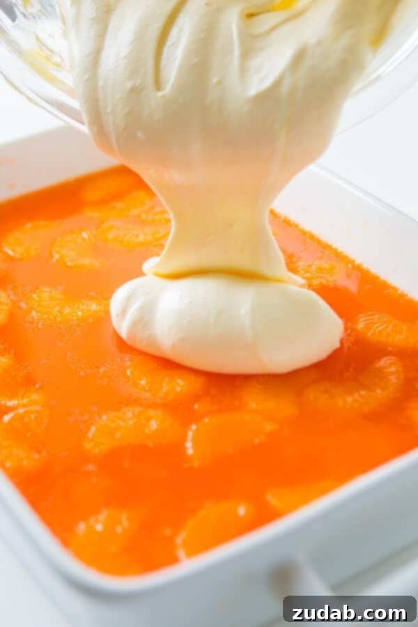 Zesty Lemon Mandarin Gelatin Delight 2 pouring cool whip topping over pan of jello salad