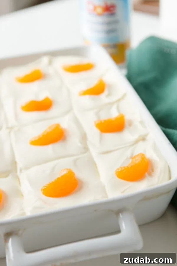 A classic Lemon Mandarin Orange Jello Salad, perfect for holiday meals, featuring a bright orange gelatin base and a creamy lemon topping. orange jello fruit salad in white baking dish