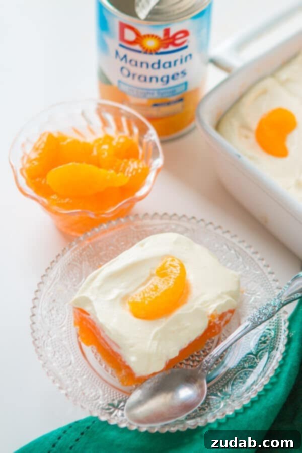 A classic Lemon Mandarin Orange Jello Salad, perfect for holiday meals, featuring a bright orange gelatin base and a creamy lemon topping. jello mandarin orange salad on glass plate with spoon