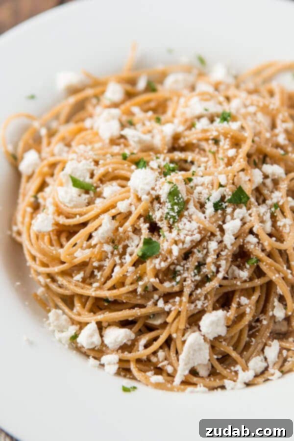 A dish of Old Spaghetti Factory Mizithra Cheese and Browned Butter Spaghetti, with a fork twisted with pasta. The golden brown butter and mizithra cheese are clearly visible on the whole wheat spaghetti. ohsweetbasil.com