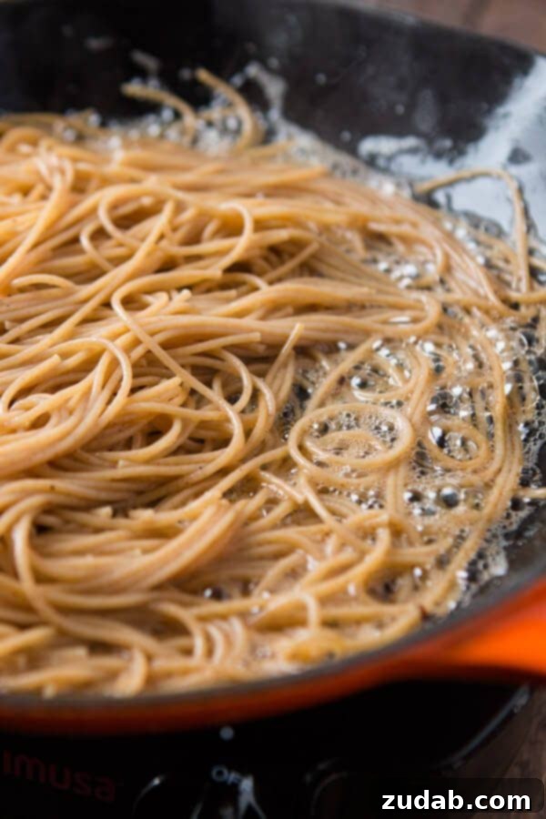 A rustic wooden spoon resting in a bowl of Old Spaghetti Factory Mizithra Cheese and Browned Butter Spaghetti, highlighting the rich texture of the browned butter and the fine crumbs of mizithra cheese. ohsweetbasil.com