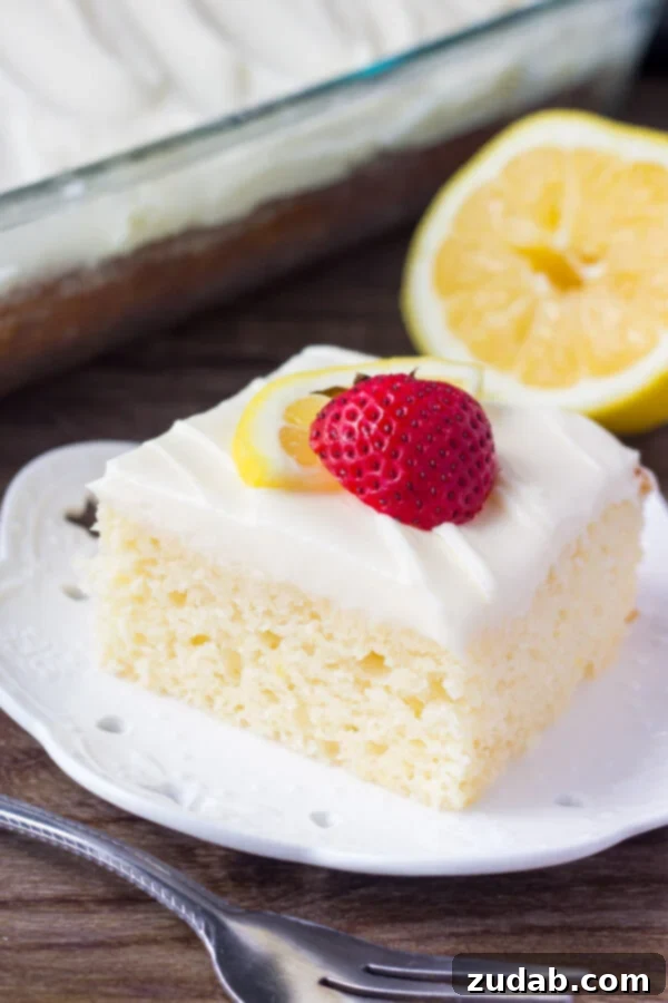 This lemon cake with lemon cream cheese frosting has a soft cake crumb and delicious lemon flavor. The cream cheese frosting is smooth & creamy for the perfect pairing. A perfectly portioned slice of moist lemon cake, generously topped with creamy lemon frosting, presented on a pristine white plate.