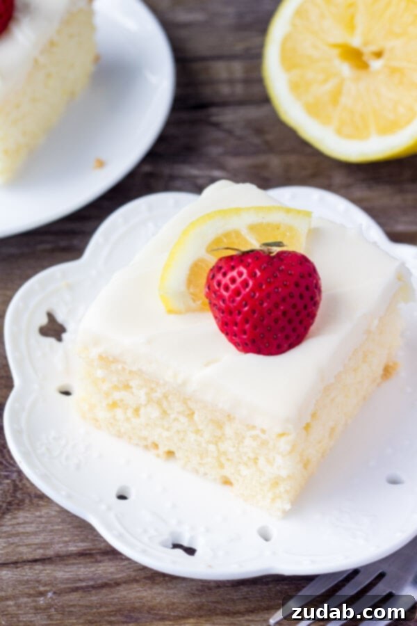 This lemon cake with lemon cream cheese frosting has a soft cake crumb and delicious lemon flavor. The cream cheese frosting is smooth & creamy for the perfect pairing. A delightful slice of homemade lemon cake, featuring a tender crumb and crowned with luscious lemon cream cheese frosting, served on a white plate.