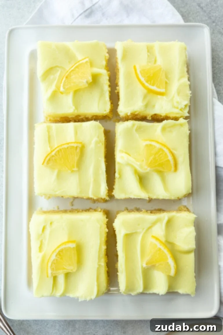 Zesty Lemon Cake with Lemon Cream Cheese Frosting 3 Several square slices of moist lemon cake, each topped with zesty lemon cream cheese frosting and a small slice of fresh lemon, arranged on a serving tray.