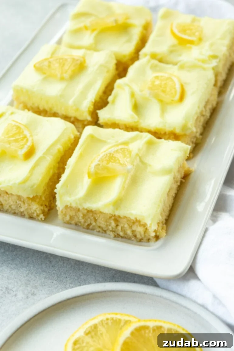 Zesty Lemon Cake with Lemon Cream Cheese Frosting 5 Several slices of moist lemon cake, each generously topped with light yellow lemon cream cheese frosting and garnished with a small lemon wedge.