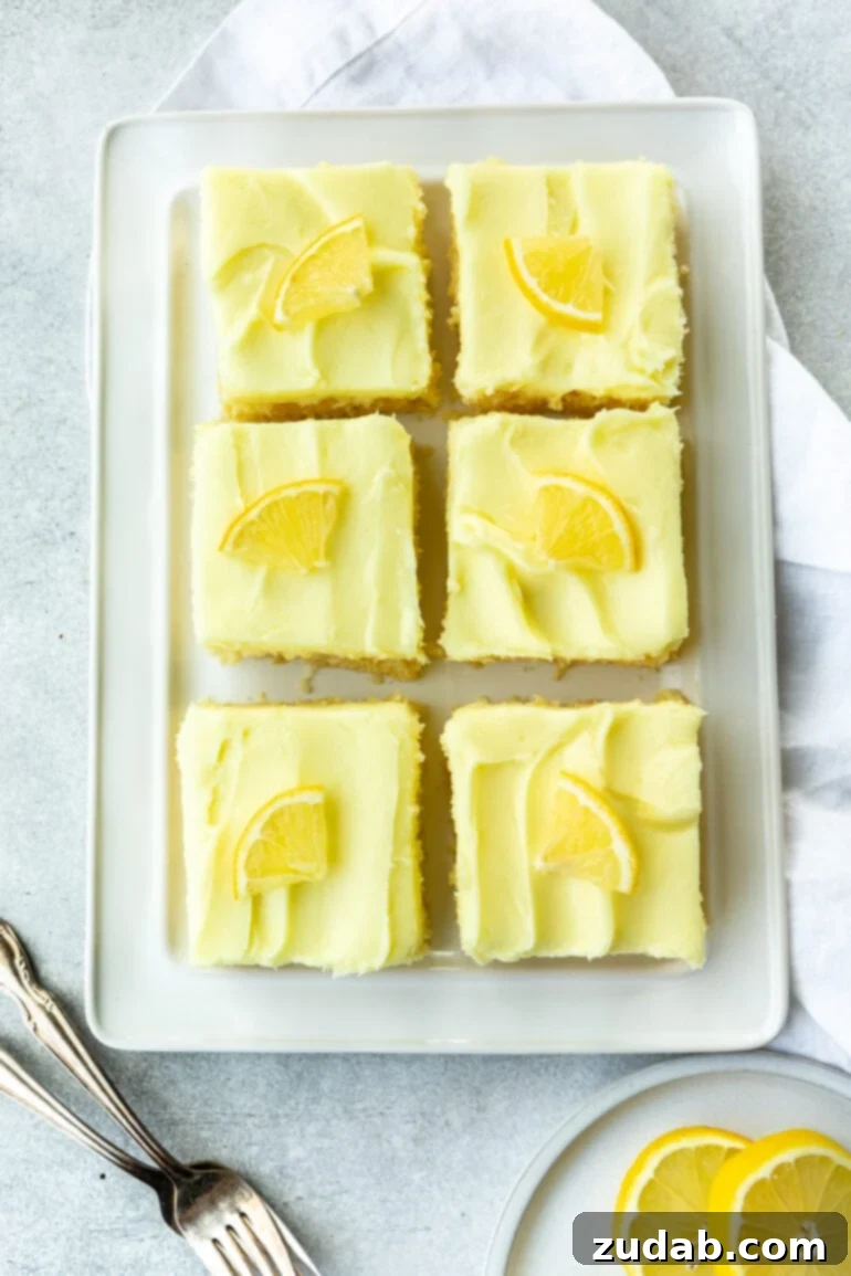 Zesty Lemon Cake with Lemon Cream Cheese Frosting 6 An overhead view of a rectangular white serving tray featuring six perfectly cut pieces of lemon cake, each adorned with creamy lemon cream cheese frosting.