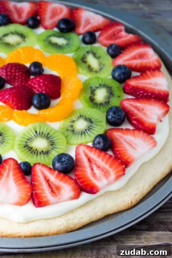 This sugar cookie fruit pizza is perfect for summer. Decorated with tangy cream cheese frosting and fresh fruit - it looks and tastes absolutely delicious. sugar cookie fruit pizza topped with assorted fresh fruit, vibrant and appealing