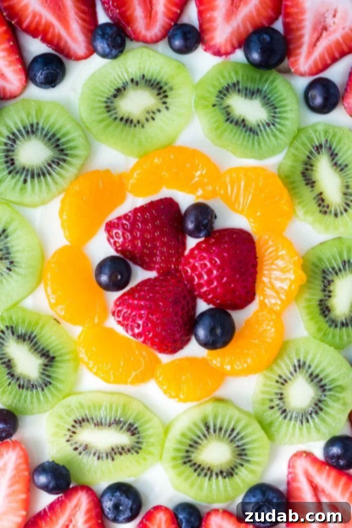 This sugar cookie fruit pizza is perfect for summer. Decorated with tangy cream cheese frosting and fresh fruit - it looks and tastes absolutely delicious. sugar cookie fruit pizza topped with assorted fresh fruit, a close-up of the beautiful arrangement