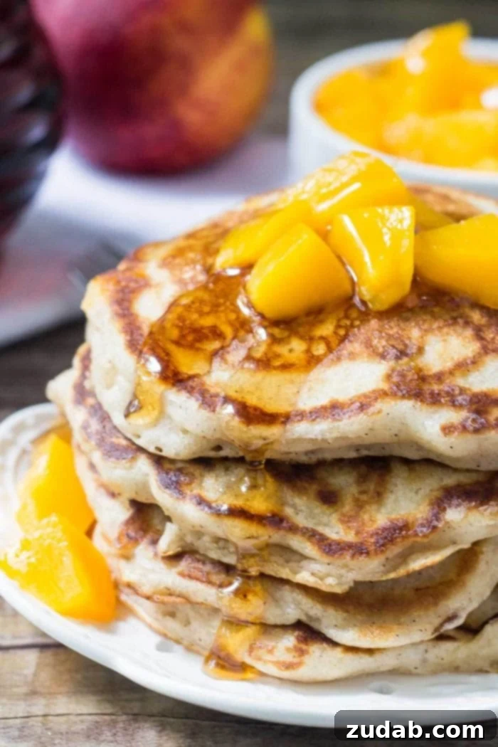 Fluffy Brown Sugar Peach Pancakes: A perfect breakfast with fresh or canned peaches. A beautifully stacked tower of golden brown sugar cinnamon peach pancakes, adorned with fresh peach slices and a drizzle of syrup, presented on a pristine white plate.