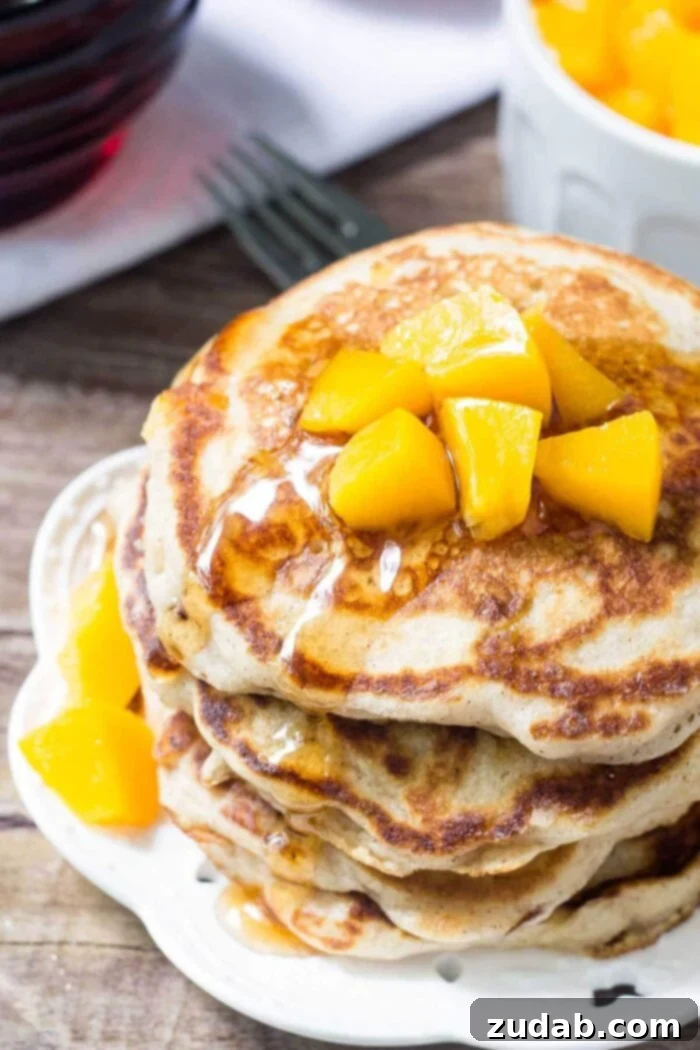 Perfectly crafted peach pancakes for a delightful breakfast or brunch. Close-up of a stack of fluffy peach pancakes, topped with fresh diced peaches, on a white plate ready to be served.