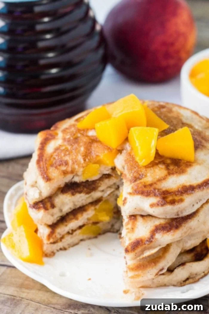 Beautifully sliced peach pancakes, showcasing their fluffy texture and peach filling. A stack of golden brown sugar cinnamon peach pancakes, cut open to reveal the fluffy interior and juicy peach pieces, on a white plate.