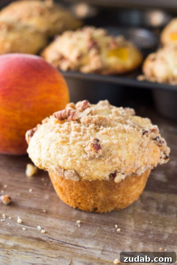 Fluffy, buttery, super soft Peach Muffins with a crunchy cinnamon-pecan streusel topping, showcasing fresh peaches.