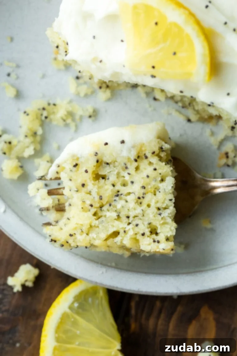 a photo of a bite of lemon poppy seed cake sitting on a fork laying on a plate next to a slice of the cake