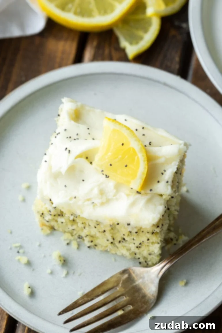 a photo of a slice of lemon poppy seed cake topped with cream cheese frosting and small wedge of lemon.