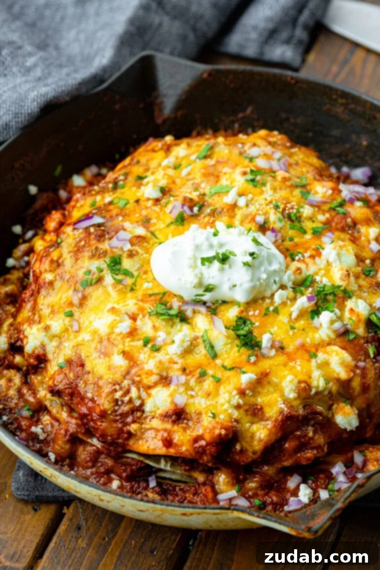 One Pan Cheesy Beef Enchilada Bake 2 a photo of a cast iron skillet full of ground beef enchilada casserole topped with melted cheese, chopped cilantro and a dollop of sour cream