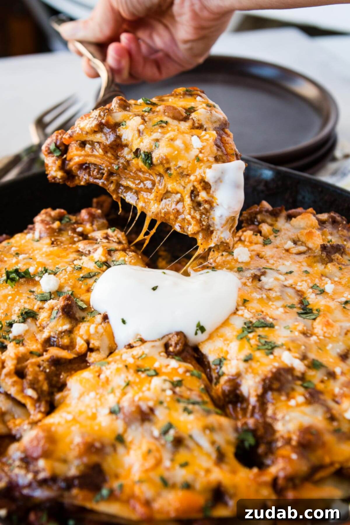 One Pan Cheesy Beef Enchilada Bake 3 a photo of someone removing a slice of enchilada casserole from a cast iron skillet