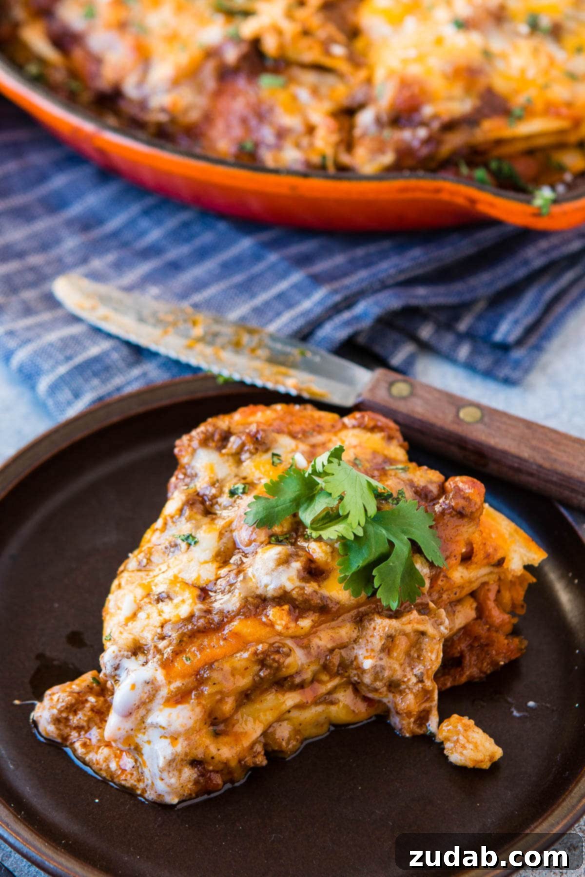 One Pan Cheesy Beef Enchilada Bake 8 a photo of a slice of enchilada casserole on sitting on a dinner plate topped with a few leaves of fresh cilantro