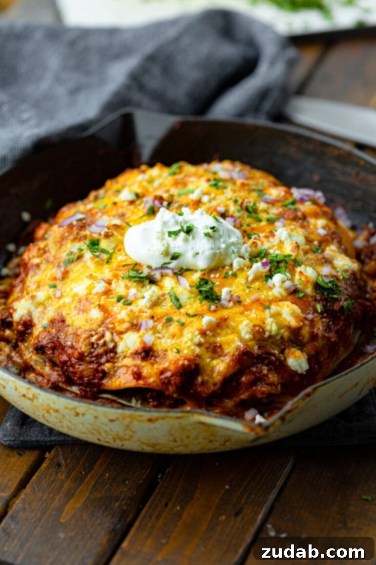 One Pan Cheesy Beef Enchilada Bake 9 a photo of a large cast iron skillet full of layers of ground beef enchilada casserole topped with melted cheese and a dollop of sour cream