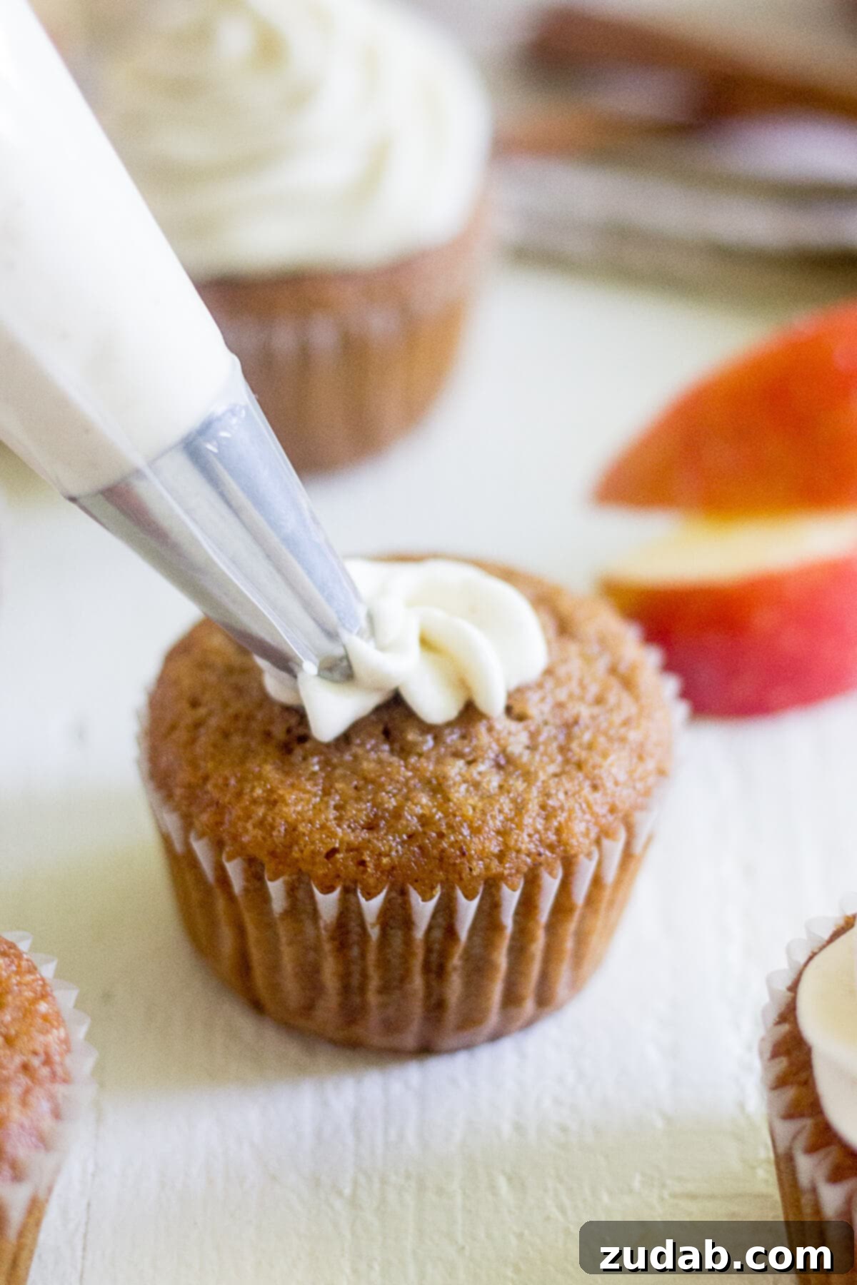 Warm Apple Cider Cupcakes with Spiced Cream Cheese Frosting 3 piping cream cheese frosting onto an apple cupcake