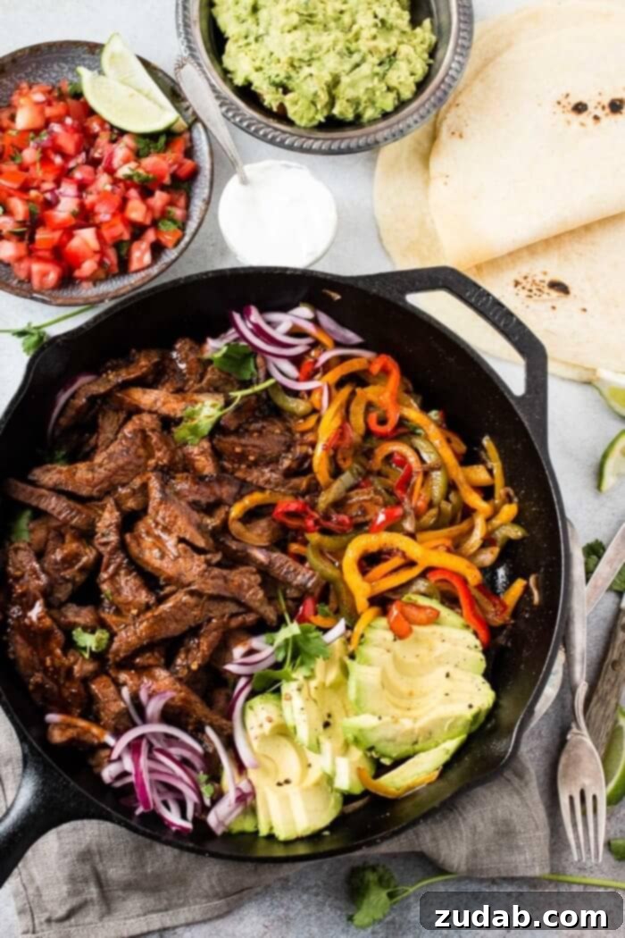 Our Secret Marinade for Tender Steak Fajitas 5 Overhead view of a spread of steak fajitas with peppers and onions, tortillas, salsa, and guacamole, perfect for a family meal