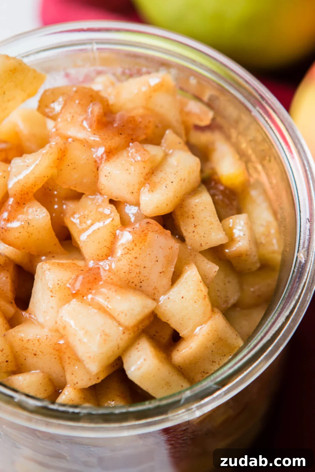 Close-up of freshly made homemade apple pie filling cooling in a glass jar, showcasing the rich texture and vibrant color of the spiced apples.