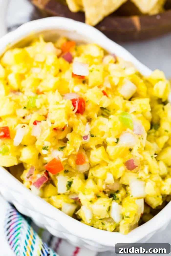 Ultimate Pineapple Salsa 4 A pristine white bowl filled with a colorful array of fresh pineapple salsa, featuring bright pineapple cubes, red and green bell peppers, fresh cilantro, and finely diced red onions, ready to be enjoyed.