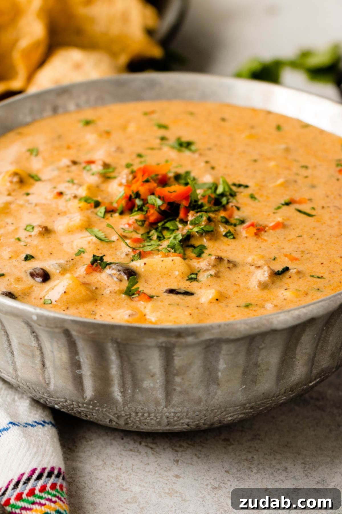 Cheesy Ground Beef Enchilada Chili 2 A vibrant bowl of Cheesy Ground Beef Enchilada Chili, garnished with fresh cilantro and a dollop of sour cream, ready to be enjoyed with multigrain tortilla chips. This easy chili recipe is perfect for a comforting meal.